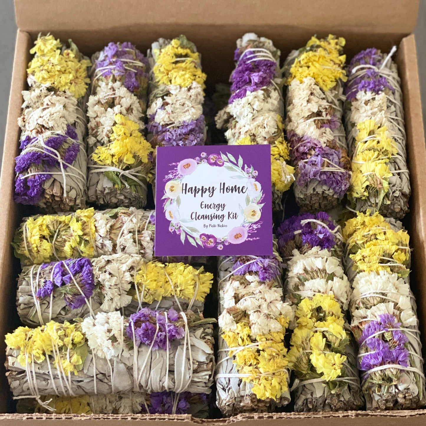 Box of 'Happy Home' energy cleansing kit with smudge sticks wrapped in yellow and purple ribbons.