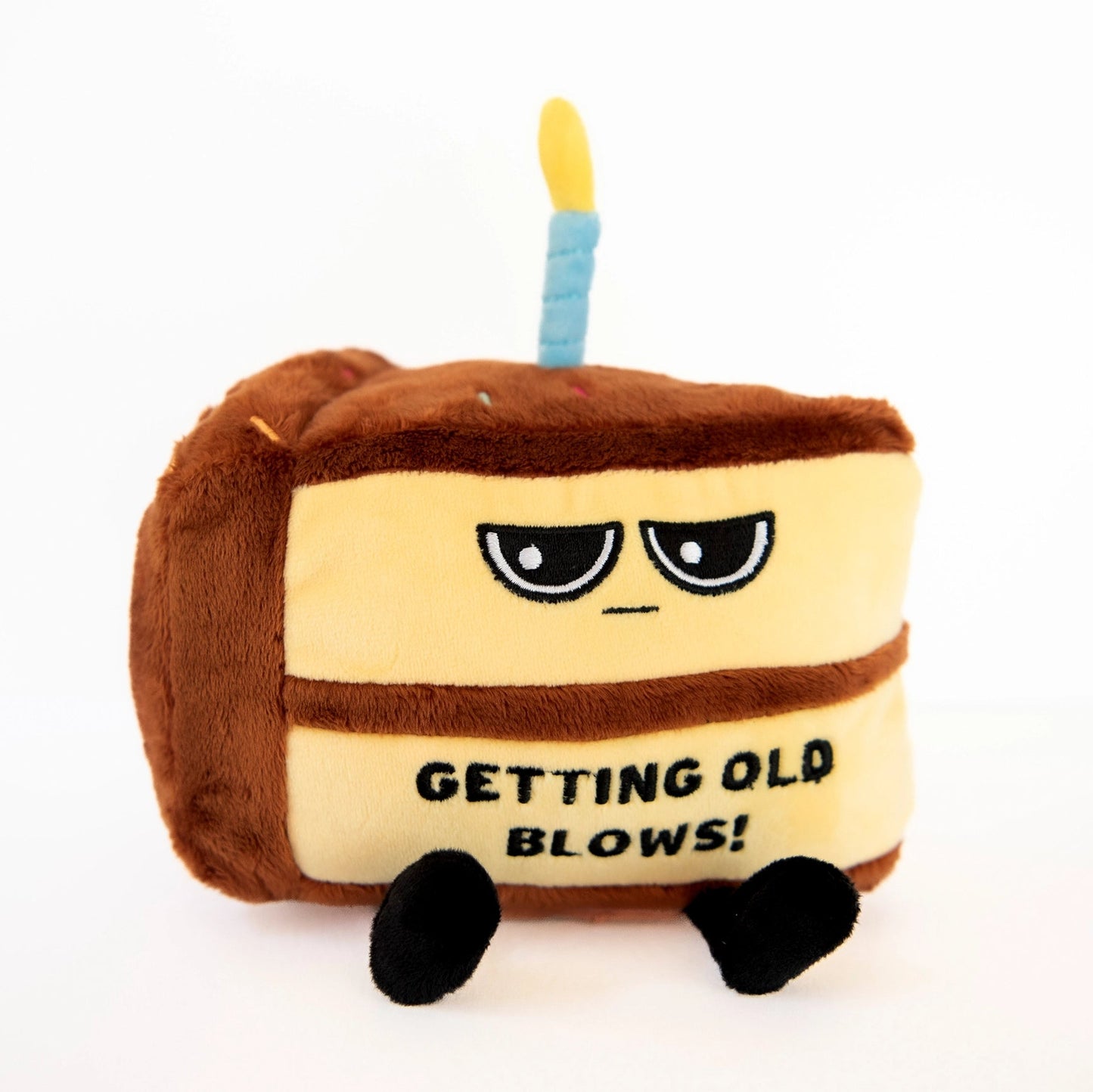 Plush toy resembling a cake with a candle and text 'Getting Old Blows!' on a white background