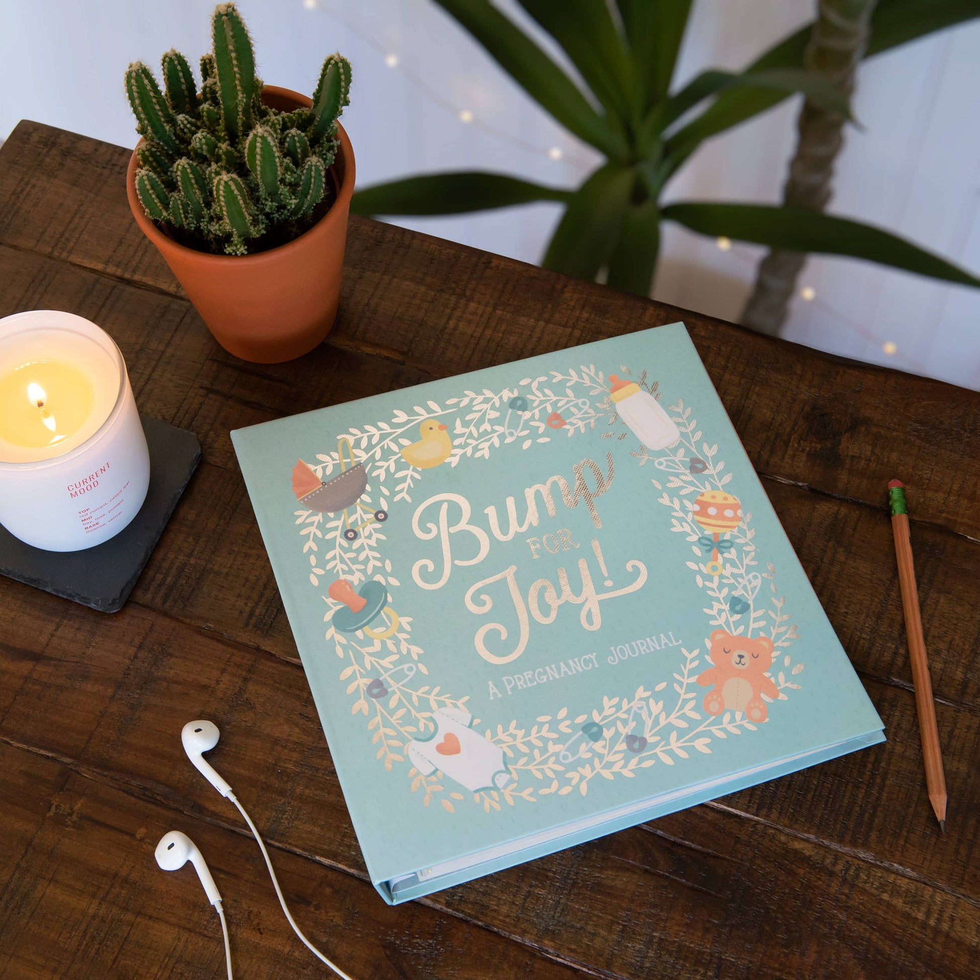 Book titled 'Bump Joy' on a wooden table with a candle, plant, and pencil.