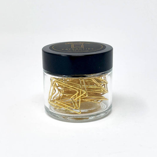 Clear jar with black lid containing gold paper clips on a white background
