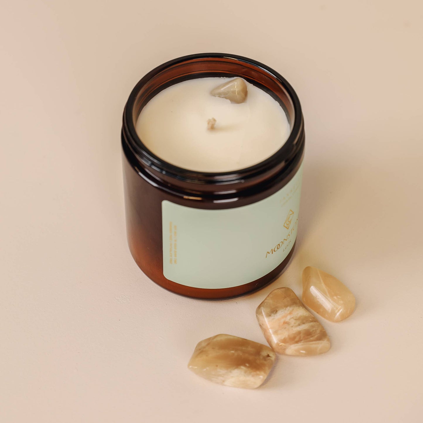 Candle in an amber jar with a label, surrounded by stones on a beige background