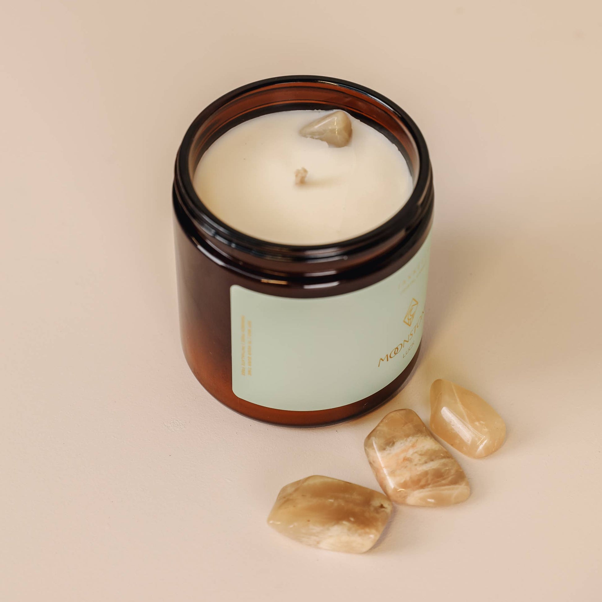 Candle in an amber jar with a label, surrounded by stones on a beige background