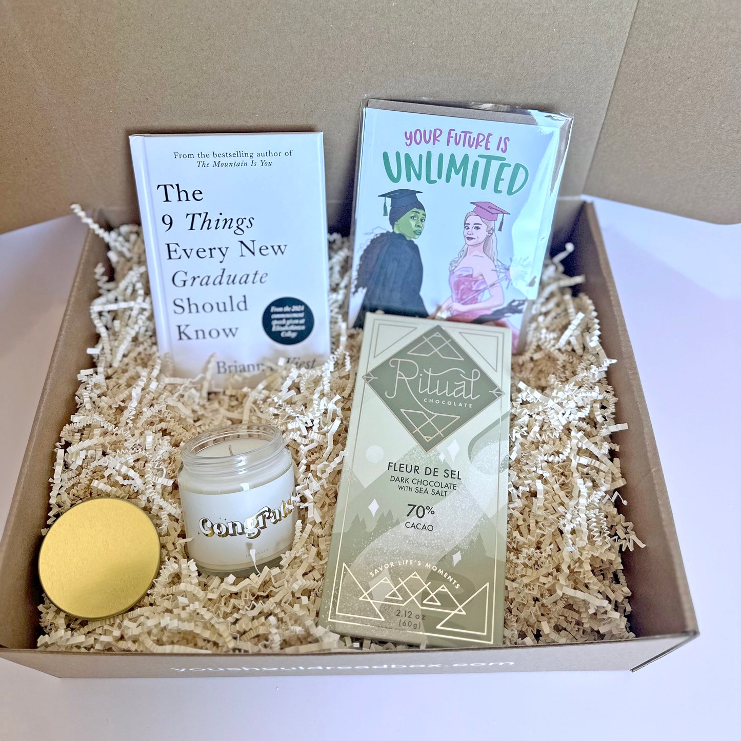 Gift box with a candle, book, chocolate bar, and books on a neutral background