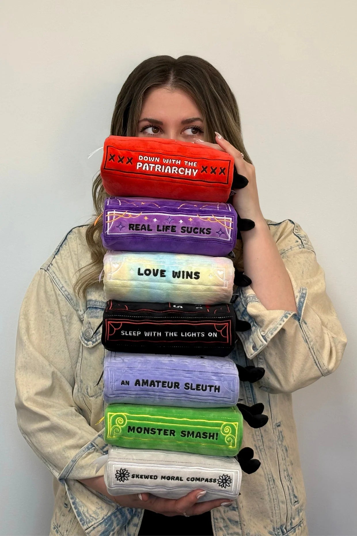 Person holding a stack of colorful plushies with text on them against a plain background