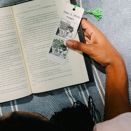Hand holding a bookmark with cartoon designs over an open book.