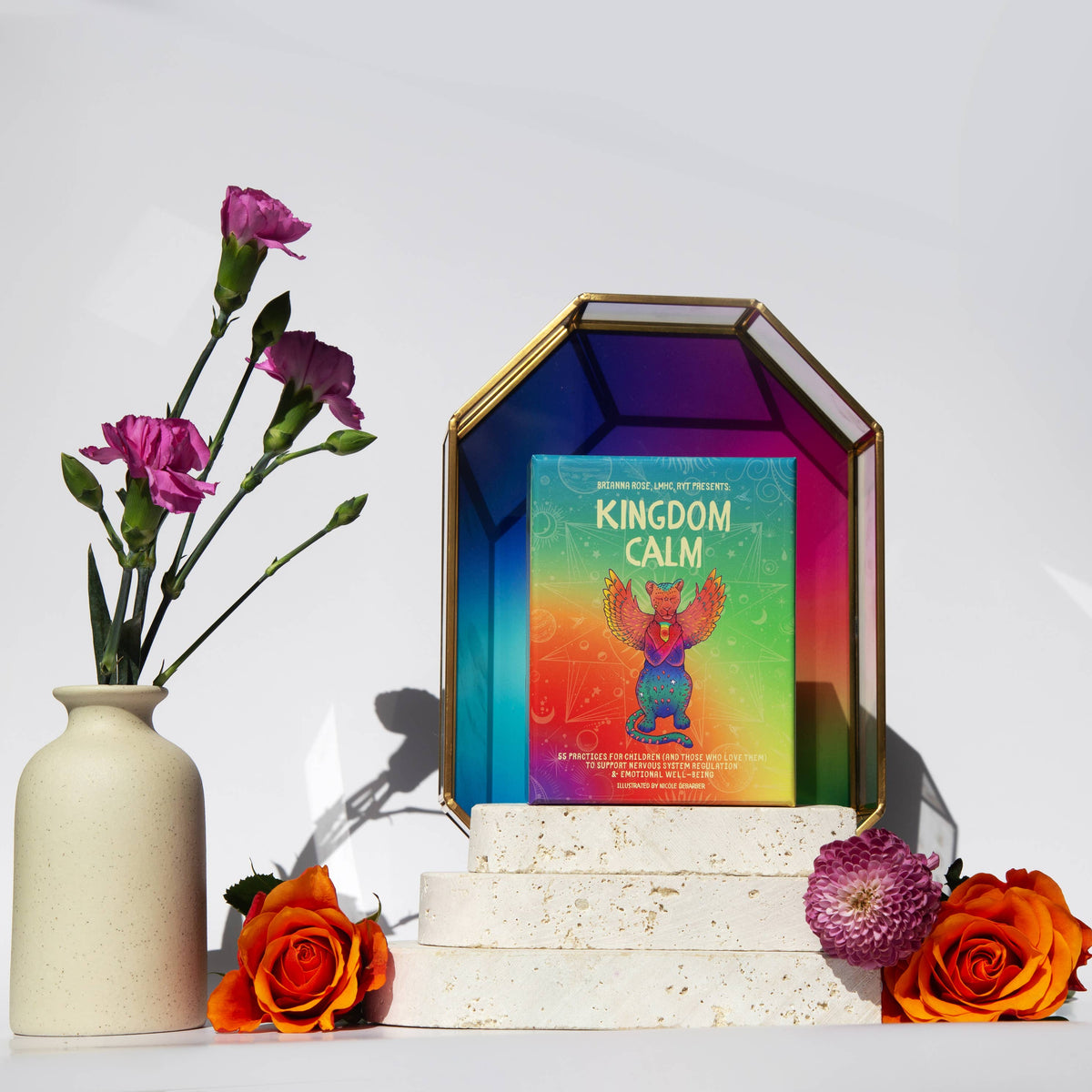 Colorful book titled 'Kingdom Calm' on a decorative stand with flowers and a vase.