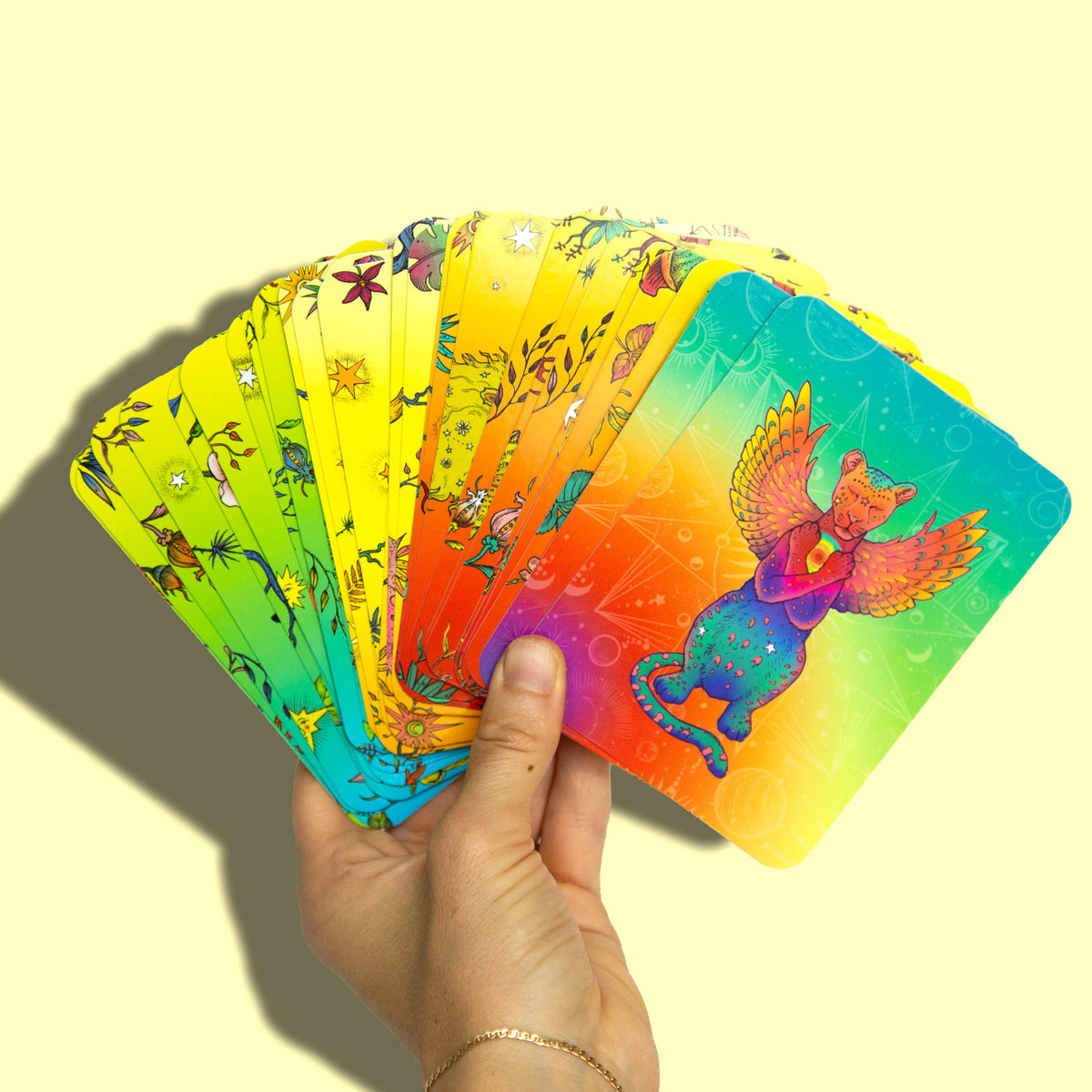 Hand holding a deck of colorful cards with a rainbow gradient on a yellow background